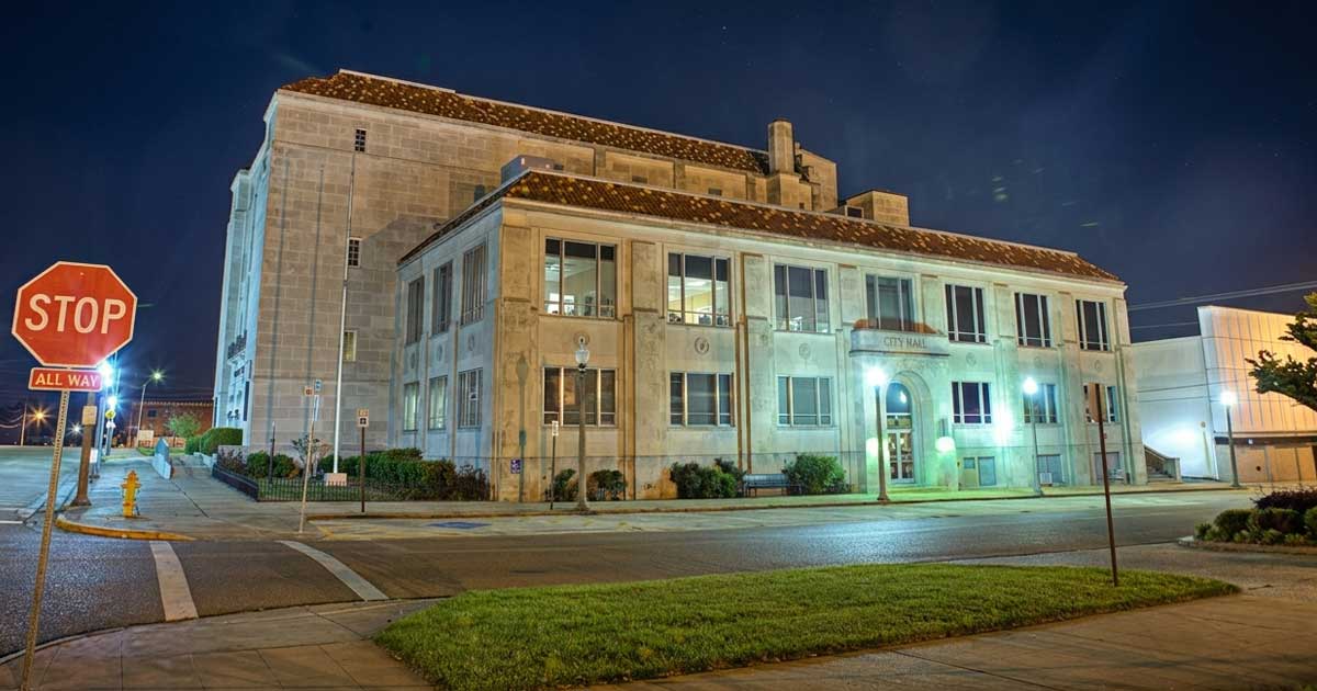 Exterior night view of the historic Texarkana, Arkansas Municipal Building and City Hall, highlighting its classic Art Deco and Collegiate Gothic stone architecture.