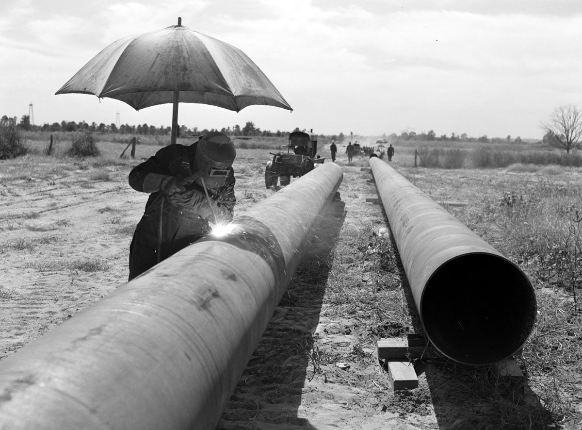 Welder under an umbrella on the Big Inch firing line, 1942