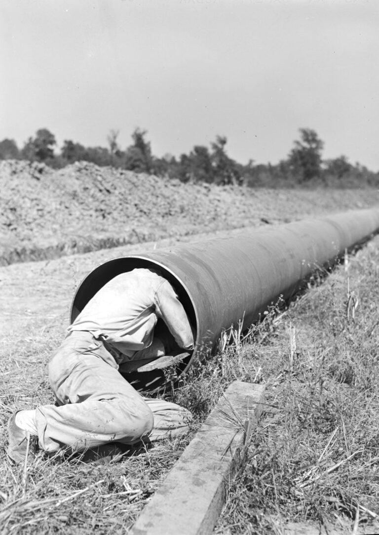 A worker slides through a section of pipe to clean out dirt before it's welded. Photo: John Vachon, Office of War Information, Library of Congress. Worker inside a section of Big Inch pipe cleaning out dirt, 1942