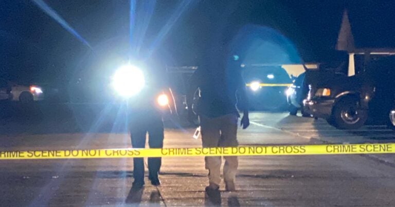 Investigators stand behind yellow crime scene tape at a nighttime scene