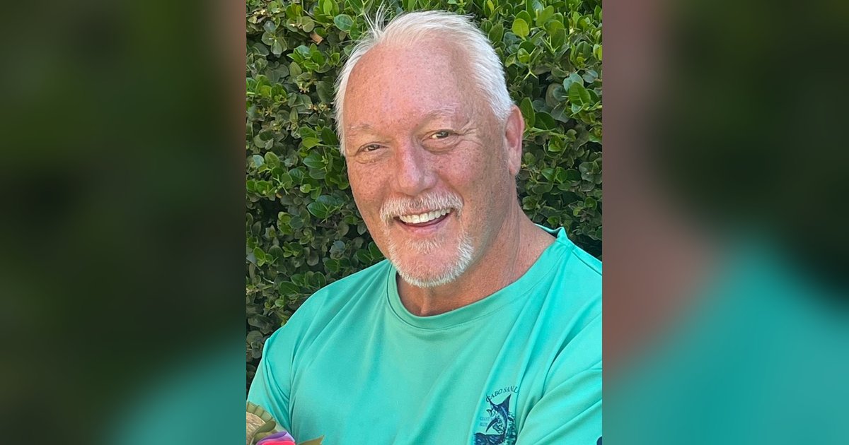 Dr. Robert Clark Green smiling in a teal shirt in front of a green hedge