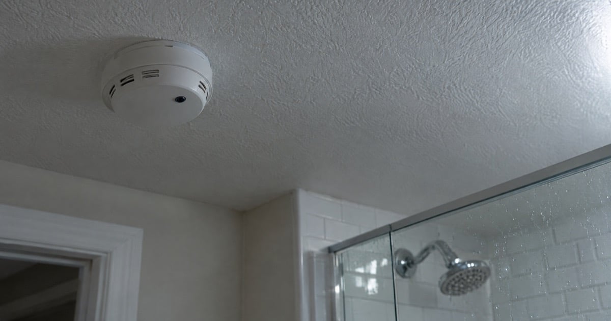 Illustration of a smoke detector with a tiny camera lens on a bathroom ceiling near a glass shower door