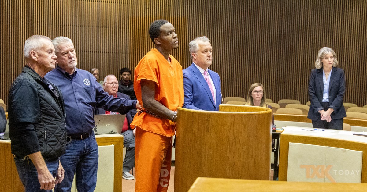 Omarion Owens in an orange jail uniform and shackles standing at the podium in a Bowie County courtroom