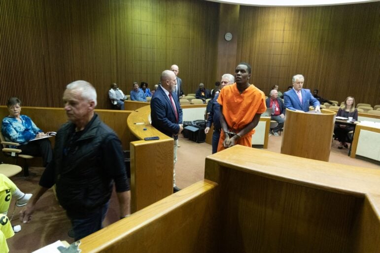 Wide view of a Bowie County courtroom with Omarion Owens in an orange jail uniform standing near the podium