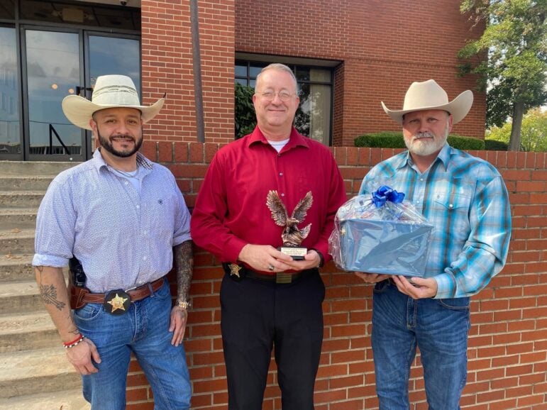 Miller County Sheriff's Office Detective Jeremy Poole holds a bronze eagle trophy outside the sheriff's office with two colleagues.