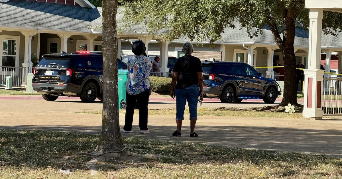 Two women watch from a sidewalk as Texarkana, Texas, police vehicles and crime scene tape sit outside an apartment complex on Stuckey Street