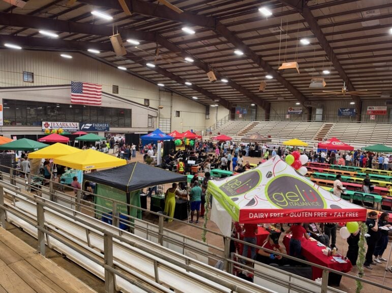 Overhead view of colorful vendor tents and long dining tables filling the Four States Fairgrounds arena