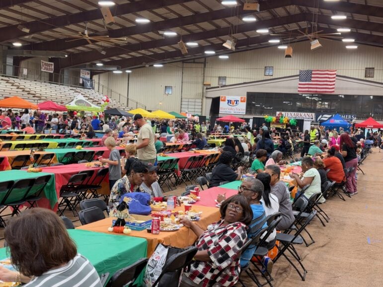 Crowd seated at long tables covered in orange and green cloths inside the fairgrounds arena