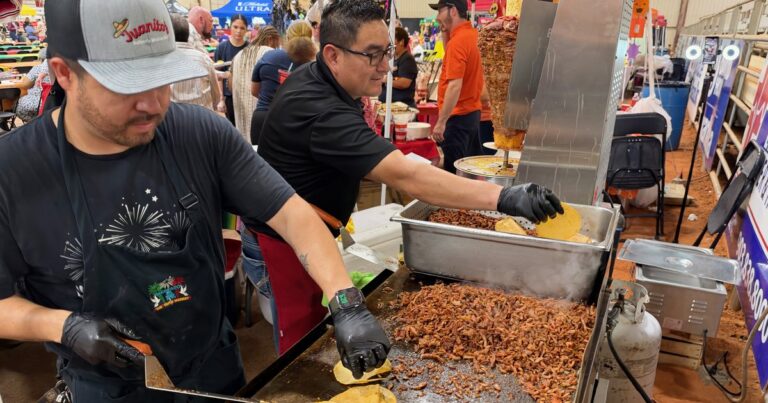 Two Juanito's cooks in black gloves flip tortillas on a flat-top grill heaped with seasoned pork