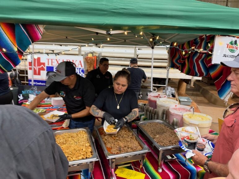 Two Juanito's workers filling food samples from steam trays under a green tent