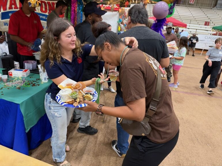Walk-On's server placing beads around a guest's neck as the guest holds a full plate